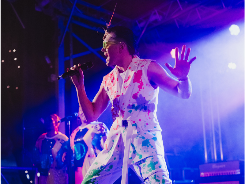 Performer singing on the WinterGlow main stage beneath colourful lighting.